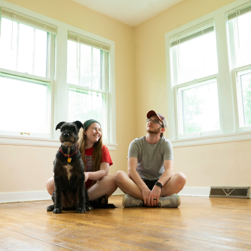 couple and dog sitting in an empty room of their new home