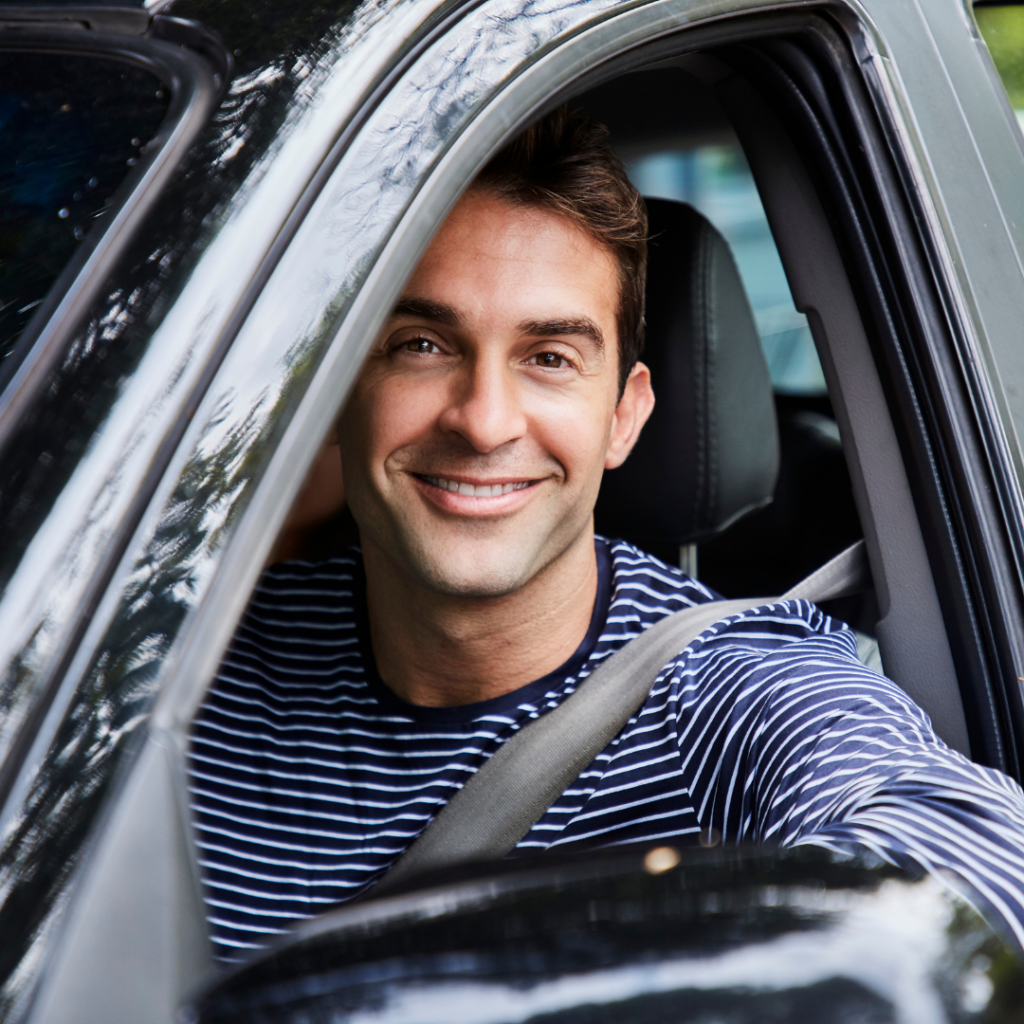 man looking out driver's side window of a car smiling